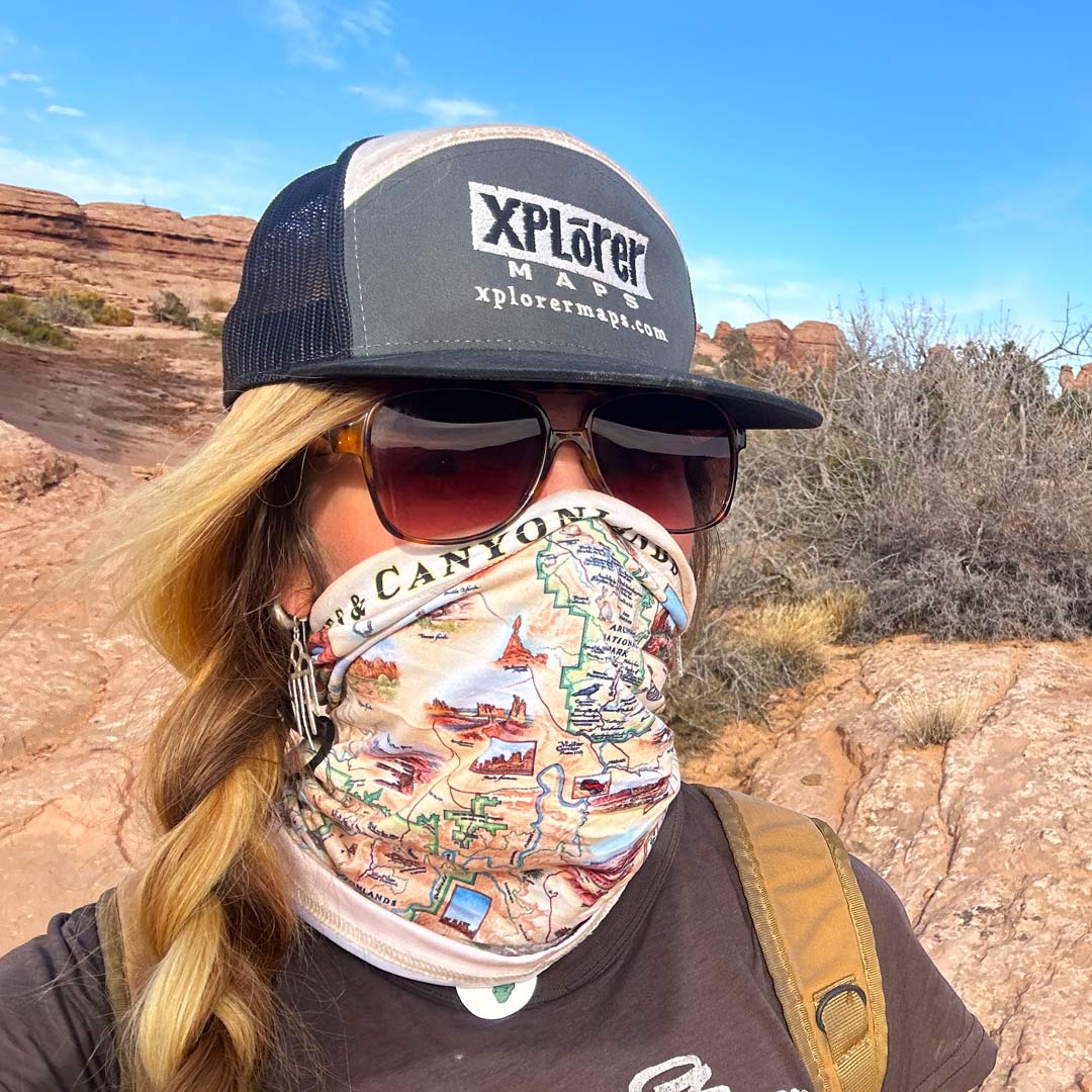 A women in Utah's Arches & Canyonlands National Park stand in front of rock formation with a gaiter cover her face.