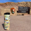 Utah's Arches & Canyonlands National Parks Map Travel Drinkware - 16 oz sitting in front of Arches National Park sign.