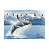 Humpback whale breaching the ocean with snow-capped mountains in the background.