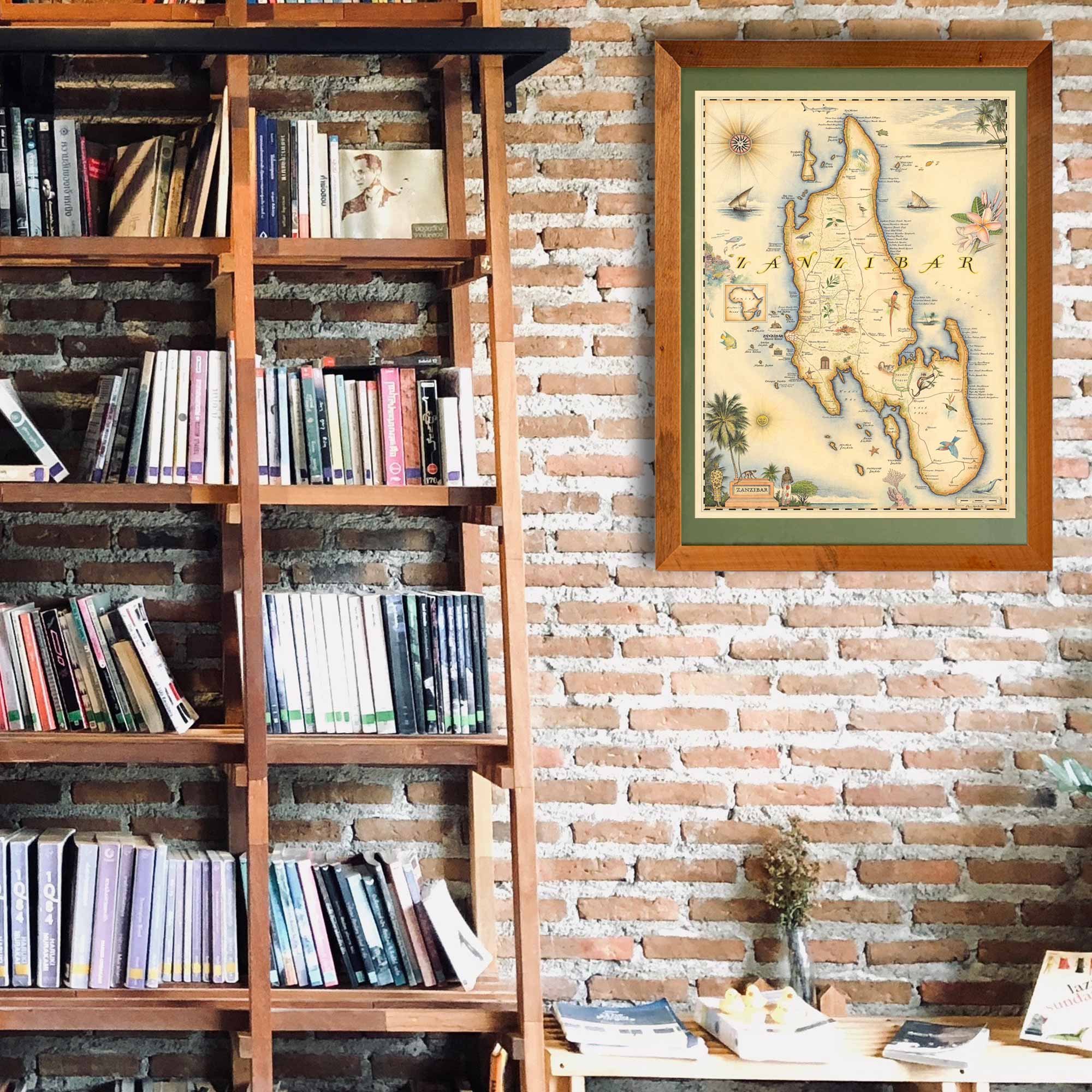 Africa's Zanzibar framed hand-drawn map is hanging on a brick wall next to a large shelf unit with a ladder.