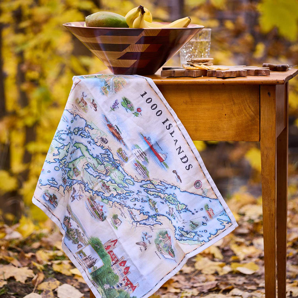 Map-themed towel on a wooden table with a bowl of fruit in an outdoor setting