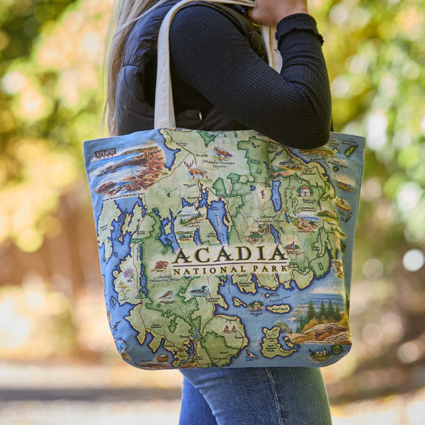 Tote bag with Acadia National Park map design held by a person outdoors.