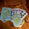 Playing cards with Acadian National Park design on a wooden surface with a leather-bound book.