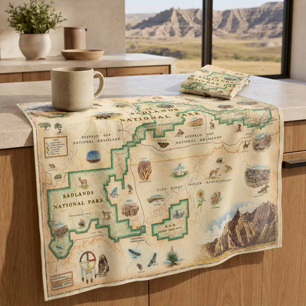A vintage-style Badlands National Park map print draped over a kitchen counter, with a matching small pouch or bag placed on top. The print features illustrated landscapes, animals, and labeled regions such as Badlands National Park and Yellowstone National Park.