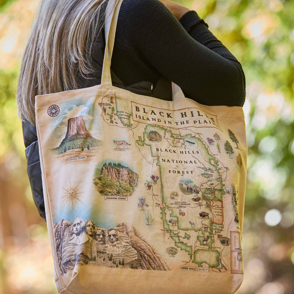 Tote bag with a map design of Black Hills National Forest held by a person outdoors.