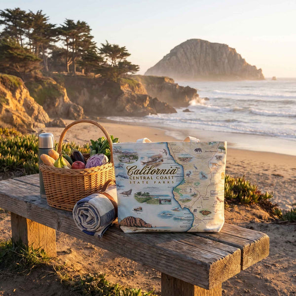Picnic setup on a wooden bench with a basket, blanket, and map of California Central Coast State Park at a beach.