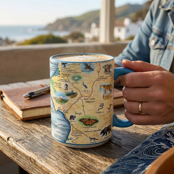 Person holding a mug with a map design on a wooden table with a scenic background