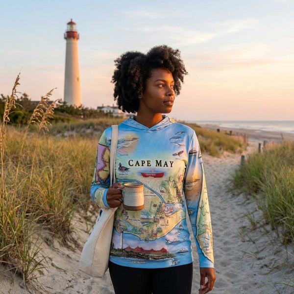 Person wearing a Cape May-themed hoodie on a beach with a lighthouse in the background