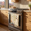 A stainless steel gas range in a warm, modern kitchen, with a decorative vintage-style map kitchen towel hanging from the oven handle.