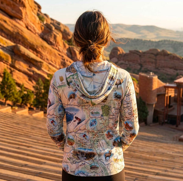Person wearing a map-patterned hoodie overlooking a scenic landscape with red rock formations.