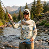 Person fly fishing in a mountainous area wearing a hoodie with a map design.