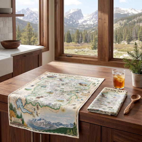 Dish towel with a map of Rocky Mountain National Park on a tablecloth, next to a glass of iced tea and a wooden spoon.