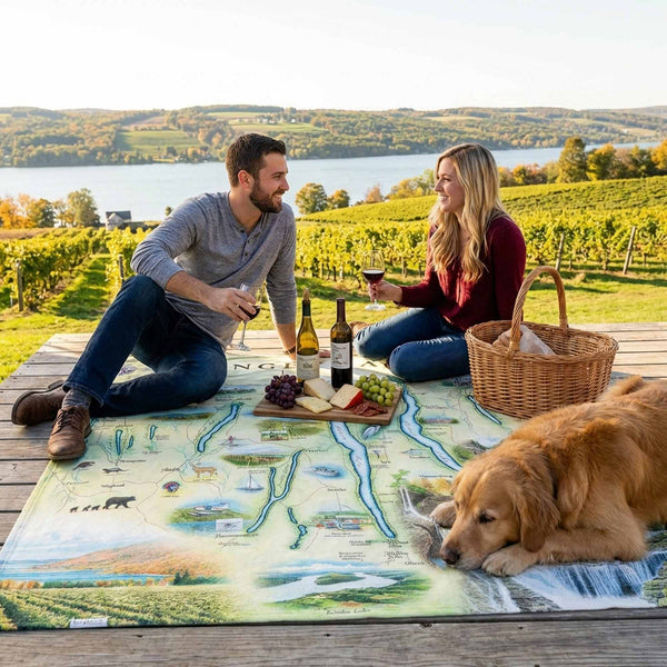 Couple enjoying a picnic with a dog on a scenic overlook with vineyards and a lake.