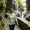 Woman standing in front of a waterfall wearing a 'Finger Lakes' sun shirt hoodie.