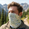 Person wearing a map-patterned face covering in a mountainous outdoor setting