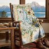Map blanket of Grand Teton National Park draped over a wooden chair with a scenic view outside.