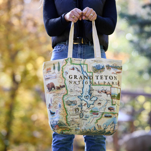 Person holding a tote bag with Grand Teton National Park design outdoors.