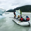 Group of people on a raft in a glacial lake with mountains in the background holding up an Inside Passage blanket

