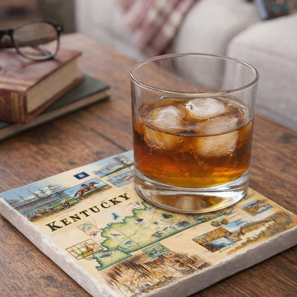 Glass of iced Kentucky bourbon on a decorative coaster with a book and glasses in the background.