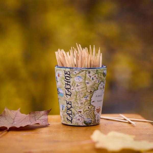 Map-themed shot glass with toothpicks on a wooden surface with autumn leaves.
