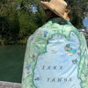 Person wearing a map of Lake Tahoe draped over their shoulders by a body of water.