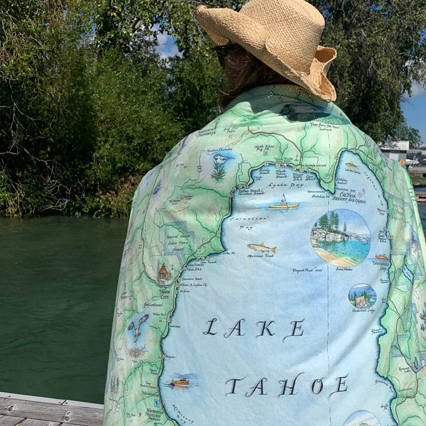 Person wearing a map of Lake Tahoe draped over their shoulders by a body of water.