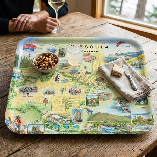Missoula Map-themed tray on a wooden table with a glass of wine and a bowl of nuts.