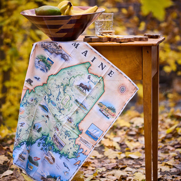 Map of Maine on a wooden table with a bowl of fruit and glass in an outdoor setting.