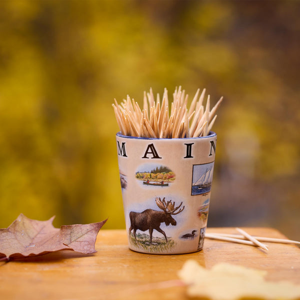 Shot glass filled with toothpicks on a wooden surface with a blurred natural background