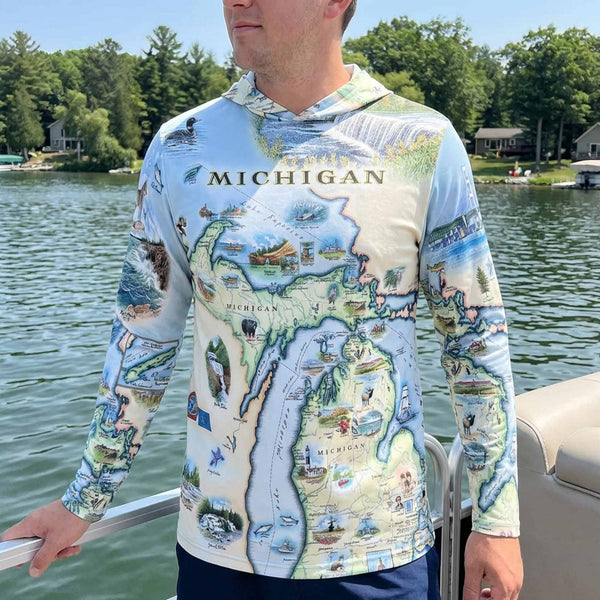 Person wearing a sun shirt hoodie with a map of Michigan design, standing on a boat by a lake.