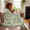 Woman sitting on a couch with a map-themed blanket, holding a mug.