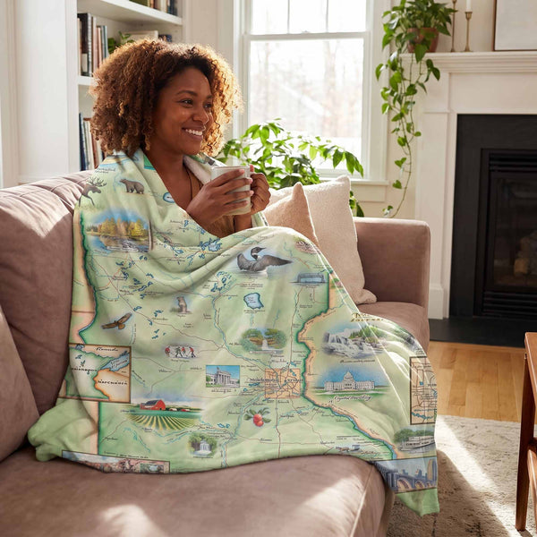 Woman sitting on a couch with a map-themed blanket, holding a mug.
