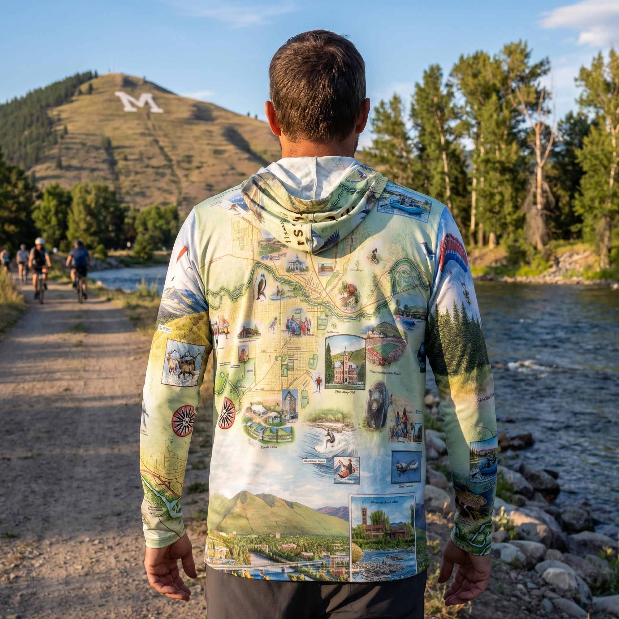 Person wearing a colorful hoodie with scenic designs, standing by a river with people in the background.