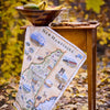 Map of New Hampshire on a wooden table with a bowl of fruit and glass in an autumn setting.