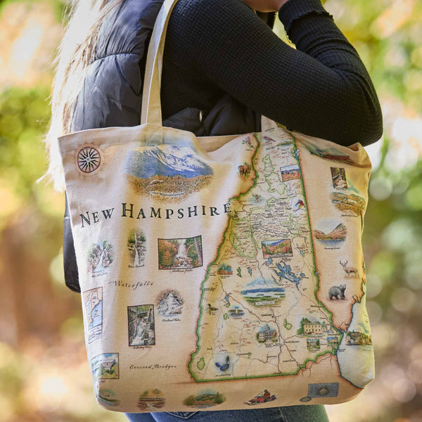 Person holding a tote bag with a map of New Hampshire design.