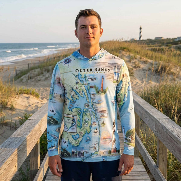 Man wearing a 'Outer Banks' themed shirt standing on a wooden boardwalk with a beach background.