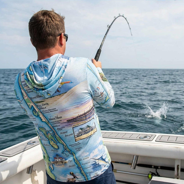 Man on a boat wearing a colorful hoodie with a map design, fishing in the ocean.