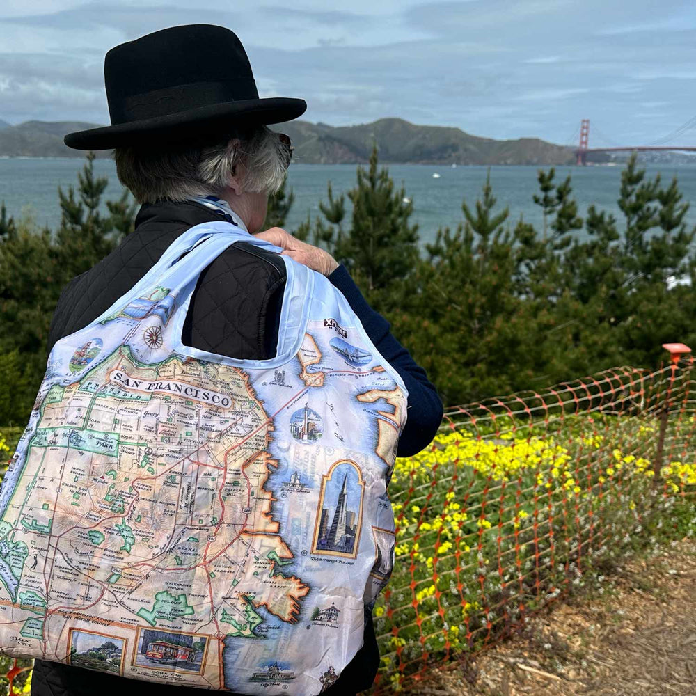 San Francisco Pouch Tote bag over the should of a women in a black hat. She is looking out at the Golden Gate Bridge.