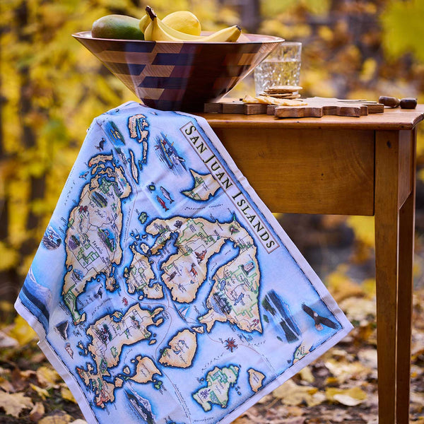 Map of San Juan Islands on a table with a bowl of fruit and glass.
