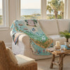 Map-themed blanket draped over a beige sofa with a coastal view through windows.