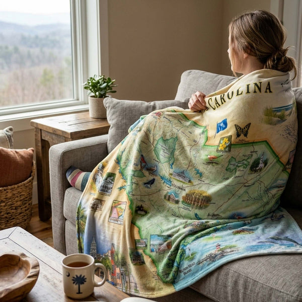 Person sitting on a couch with a scenic blanket draped over them, in a cozy living room setting.