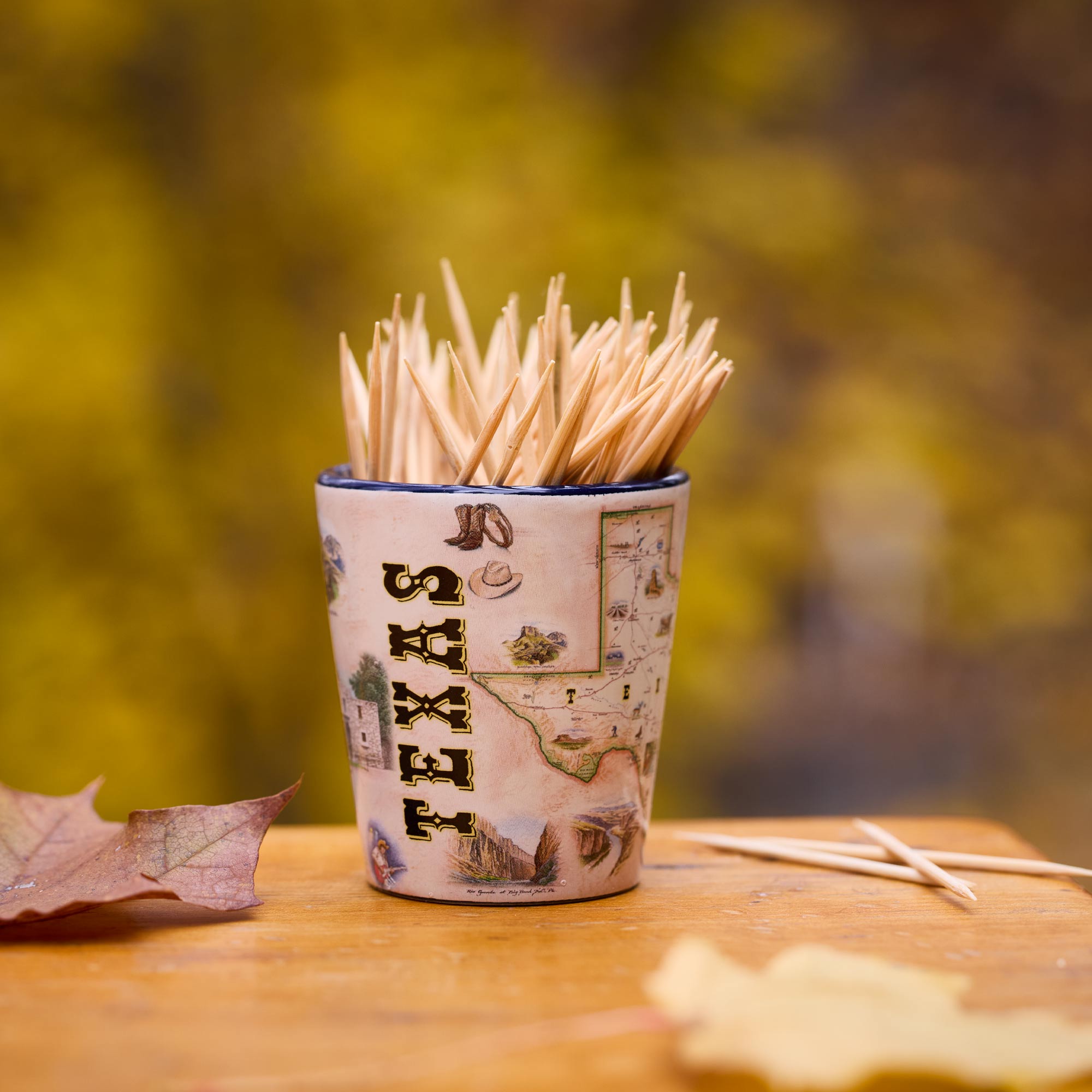 Map-themed shot glass with toothpicks on a wooden surface with a blurred natural background