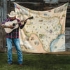Man with cowboy hat playing the guitar in front of the Texas Blanket that is hanging on a barn. 