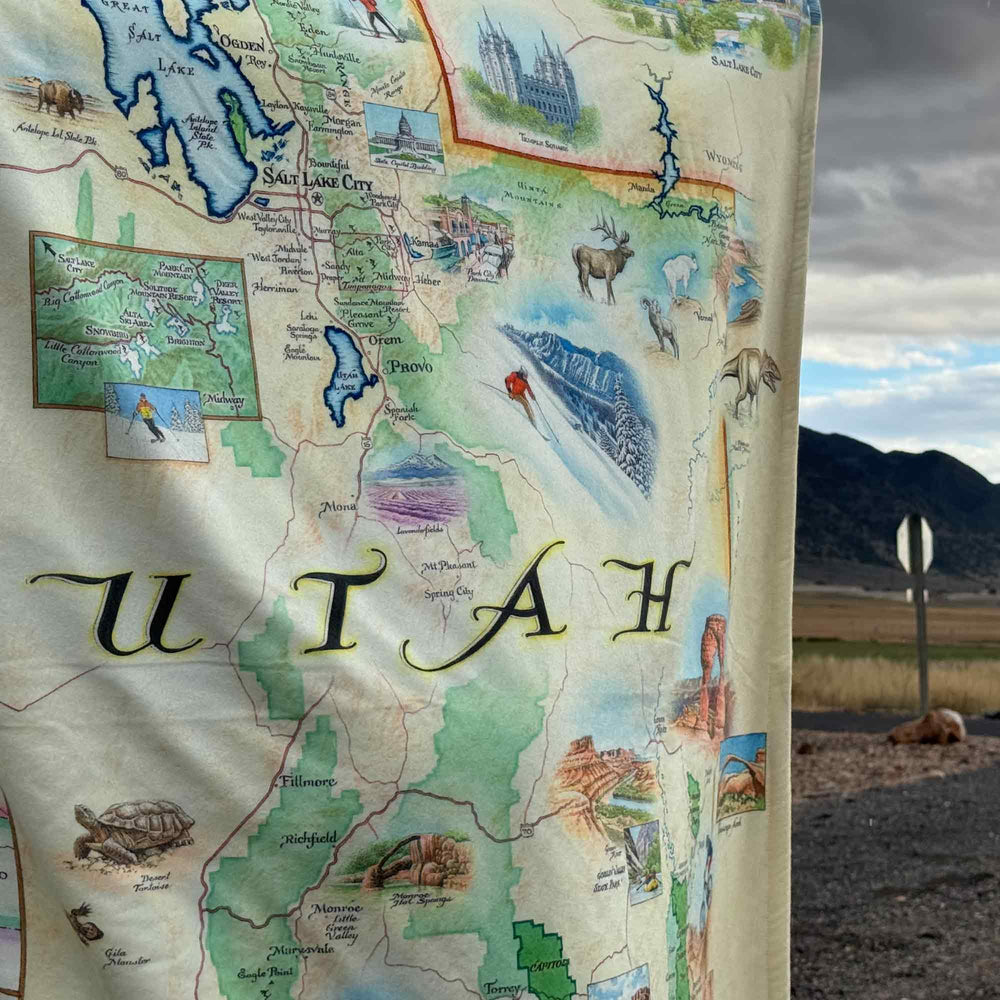 A man wearing Utah State Map fleece blanket around him. Featuring intricate details of popular cities, iconic landmarks such as Arches National Park and Bryce Canyon, and vibrant flora and fauna indigenous to the region.