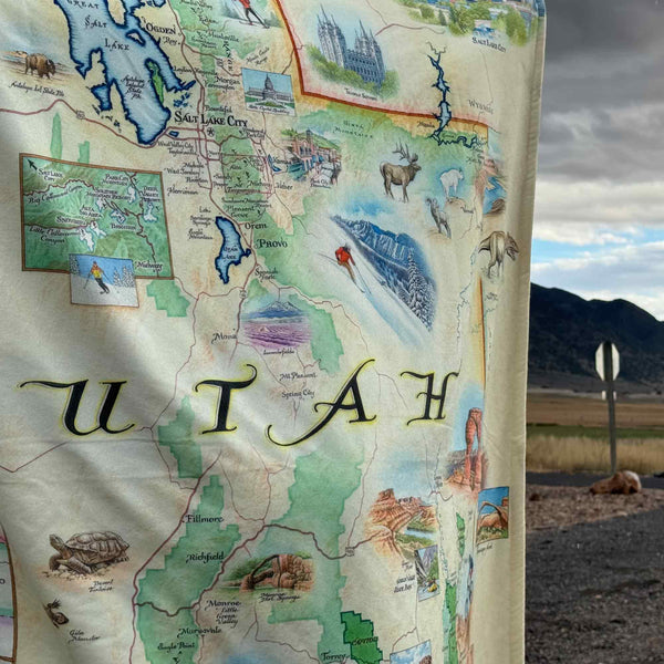 A man wearing Utah State Map fleece blanket around him. Featuring intricate details of popular cities, iconic landmarks such as Arches National Park and Bryce Canyon, and vibrant flora and fauna indigenous to the region.