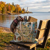 Tote bag with Wisconsin map design on a wooden bench by a lake with a lighthouse in the background.