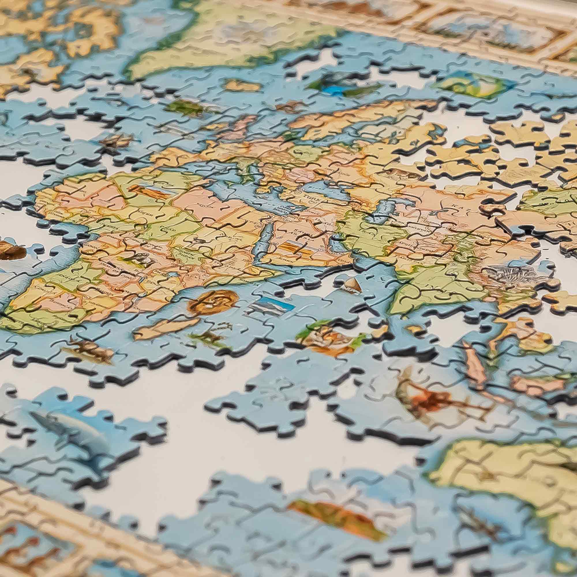 A close-up of a completed world map jigsaw puzzle, showing continents in soft beige, green, and brown tones with blue oceans. Several loose puzzle pieces are scattered around the edges.