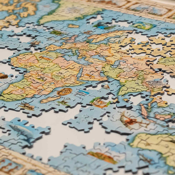 A close-up of a completed world map jigsaw puzzle, showing continents in soft beige, green, and brown tones with blue oceans. Several loose puzzle pieces are scattered around the edges.