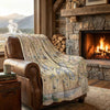 Brown leather chair with a map-themed blanket in front of a stone fireplace with a fire.