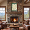 A framed vintage-style map print hangs above a stone fireplace in a rustic living room with leather sofas, a coffee table, and mountain views visible through the windows.